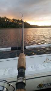 A fishing rod against the side of a boat looking toward a beautiful sunrise over Four Springs Lake